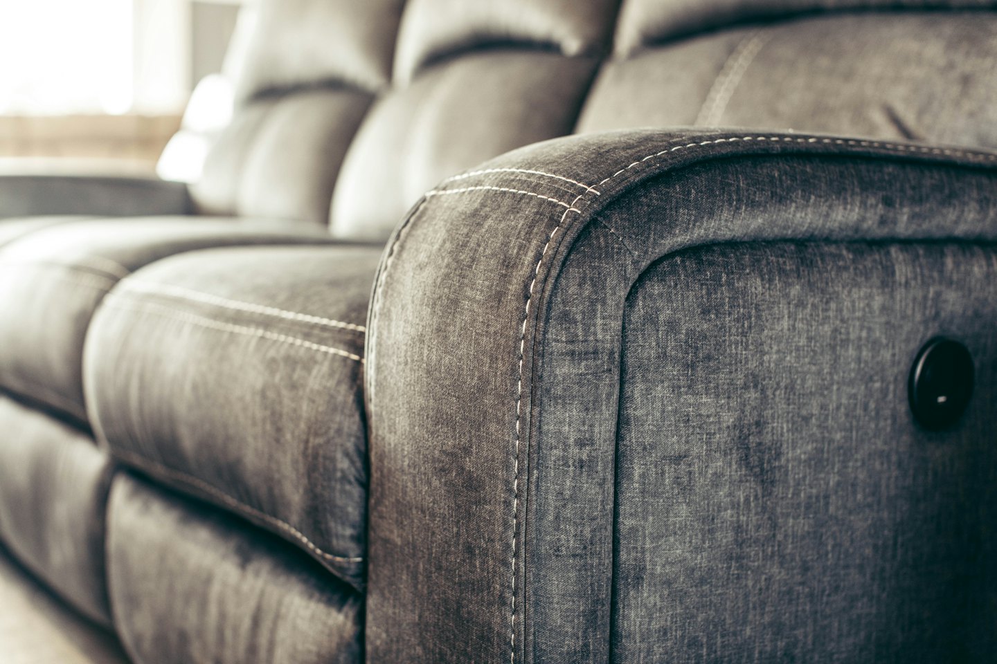 Moderner grauer Stoffsofa mit sichtbaren Nähten und Steuerung.