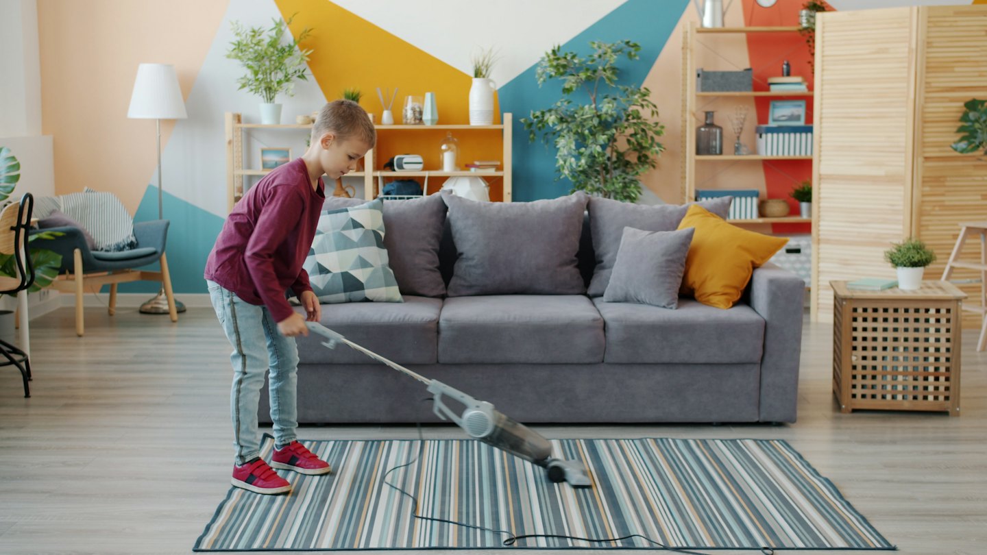 Ein Junge saugt einen gestreiften Teppich im Wohnzimmer.
