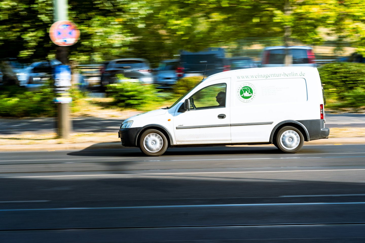 Lieferwagen mit grünem Logo fährt durch Stadtstraße.